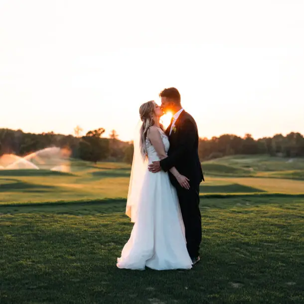 A bride and groom kissing in the grass.