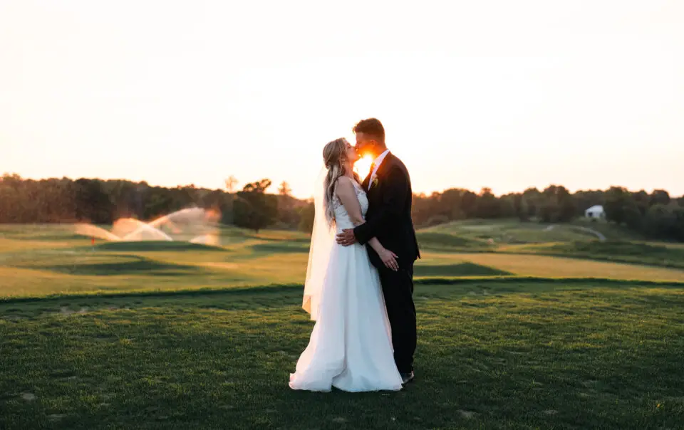 A bride and groom kissing in the grass.