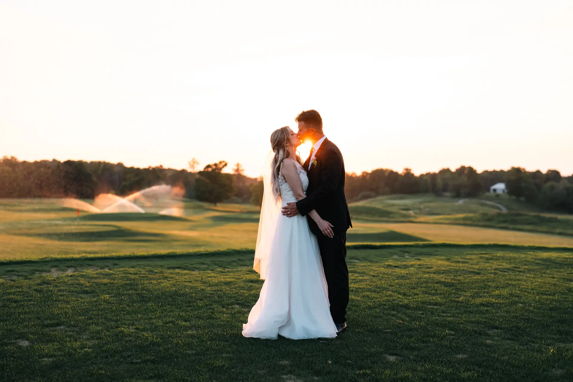 A bride and groom kissing in the grass.