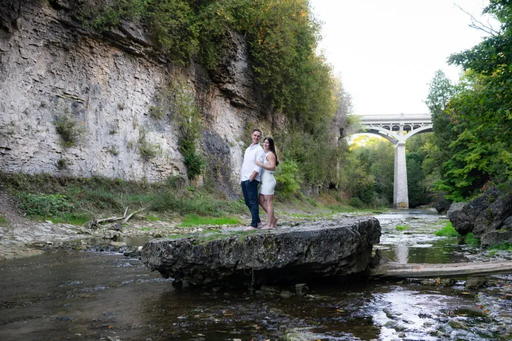 A man and woman standing on top of rocks near water.