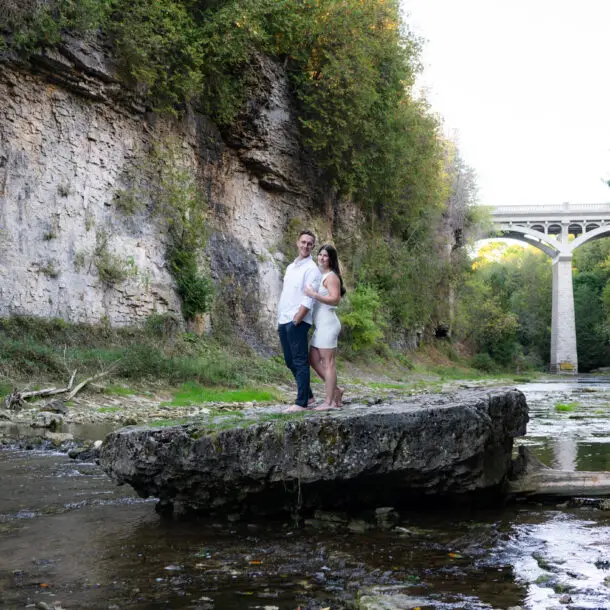 A man and woman standing on top of rocks near water.