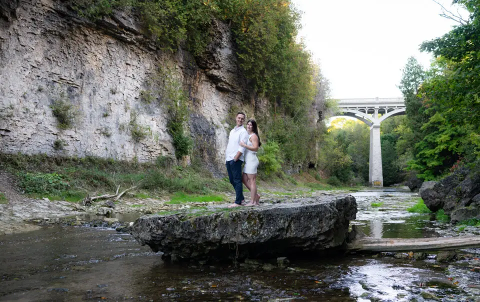 A man and woman standing on top of rocks near water.