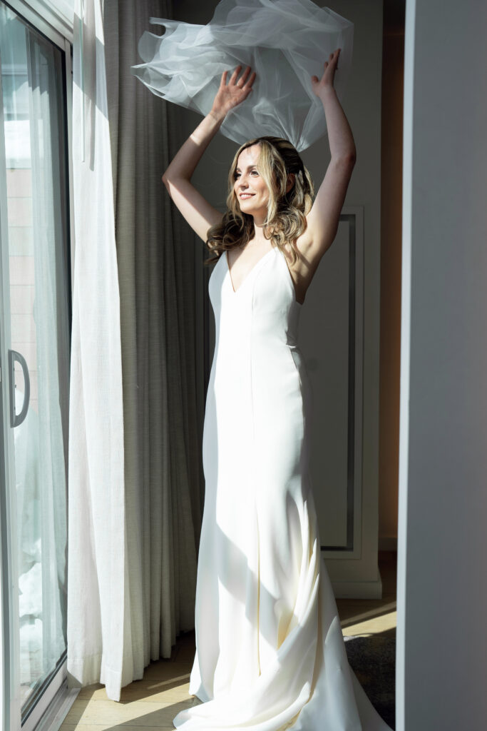 bride lifting her veil in front of window at pearle hotel burlington wedding photography pricing