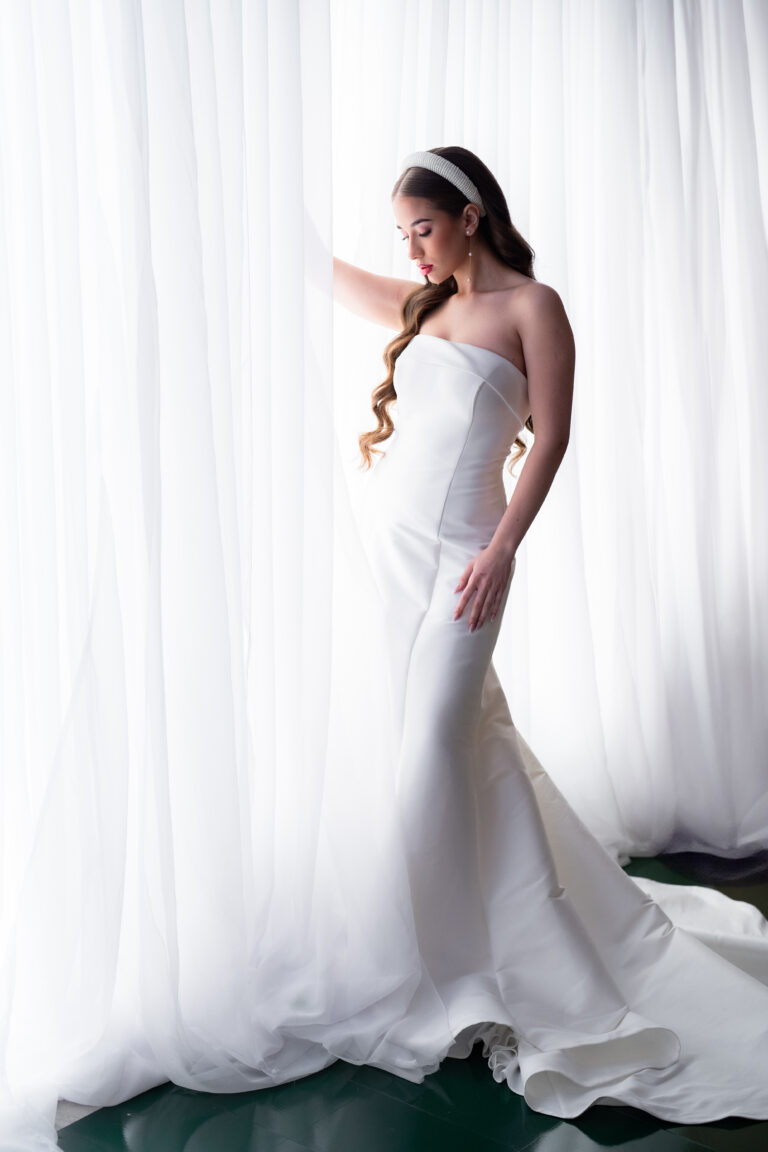 Bride looking through window with white drapes wedding photographer