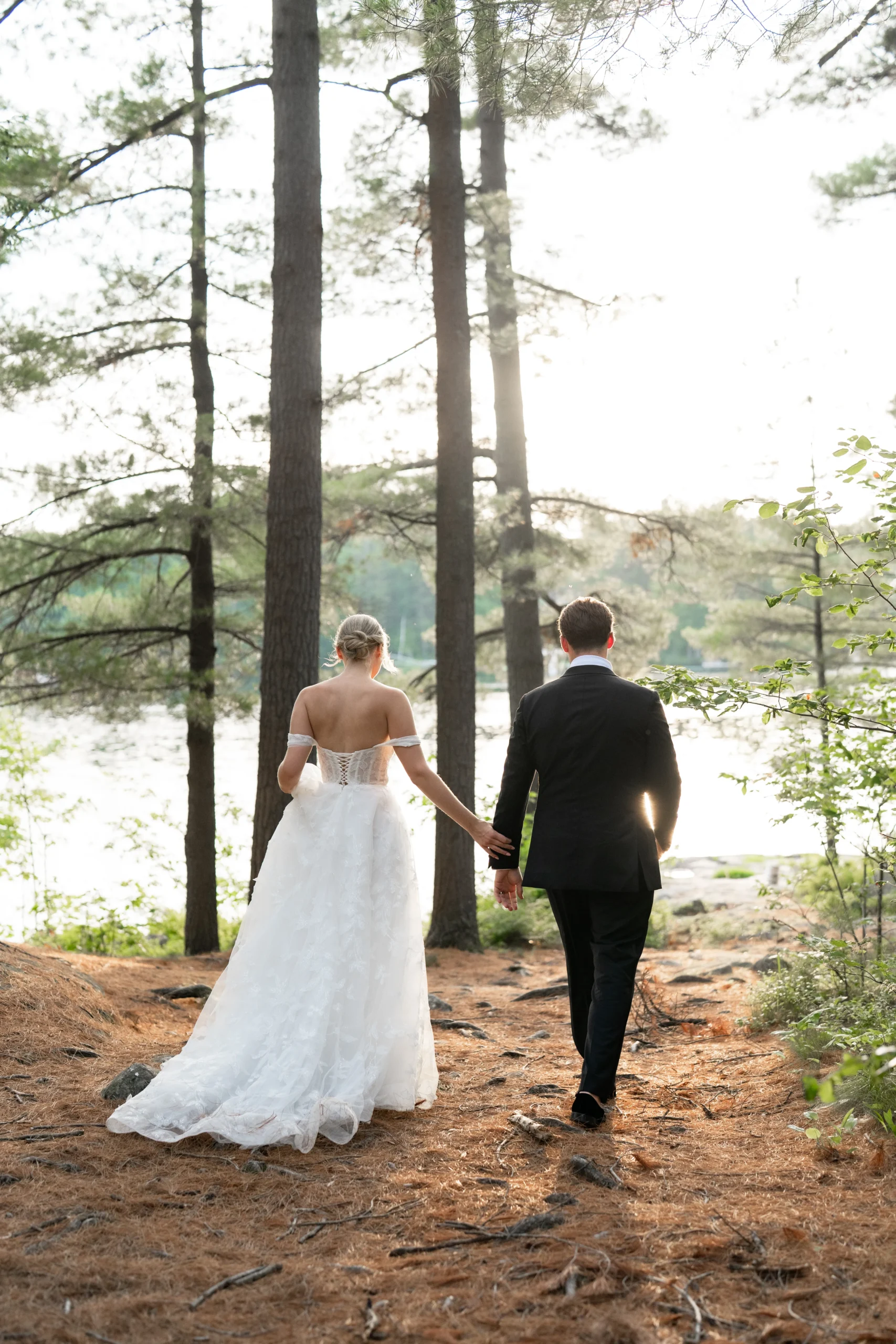 bride and groom walking toward the water in muskoka