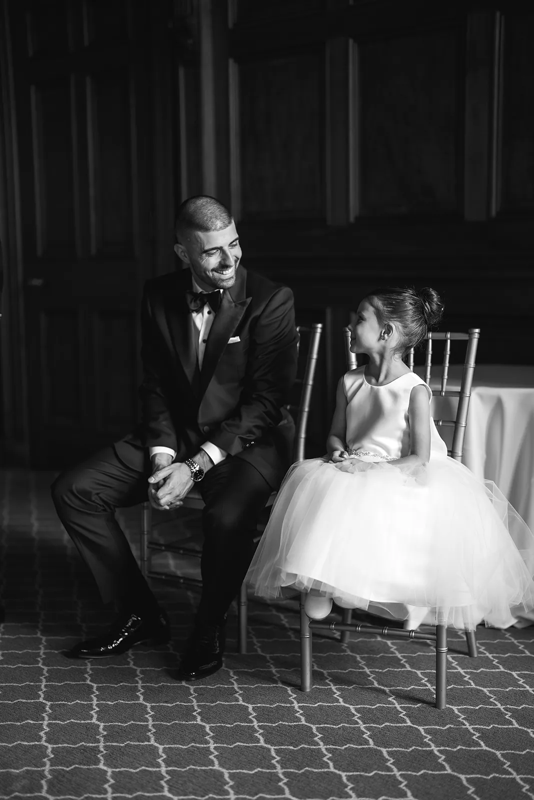 groom sitting on a chair smiling at flower girl sitting on chair in the chairmans boardroom at one king west hotel